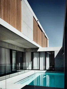 A modern residential exterior featuring concrete and wood materials, with a swimming pool.