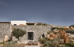 A modern house with a stone exterior and wooden accents, featuring outdoor lounging furniture and a clear blue sky.