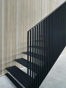 A modern steel staircase with black railings and a wooden wall on a concrete floor.