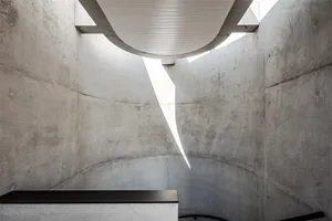 A minimalist concrete interior space with a white ceiling and a black platform.