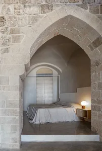 A modern minimalist bedroom featuring a concrete floor and concrete walls with an arched entryway.