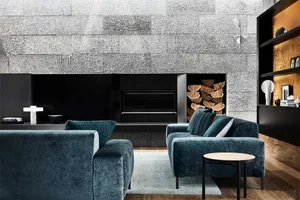 A minimalist living room with a textured metal wall, dark blue sofas, and a fireplace.