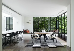A modern kitchen dining room featuring black metal chairs around a round dining table with marble top, set on a black and whi