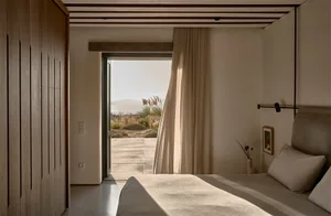 A minimalist bedroom with a bed covered in cotton sheets, overlooking a desert landscape.