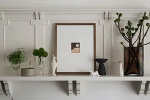 A minimalist shelf featuring a frame with a geometric abstract artwork, a small green plant, and various modern decorative it