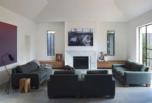 A modern living room with dark sofas, a marble fireplace, and large windows.