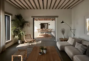A minimalist living room featuring concrete and wood materials, with a couch, coffee table, and potted plants.