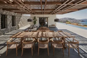 A modern residential patio with wooden furniture and a stone wall, overlooking a scenic landscape.