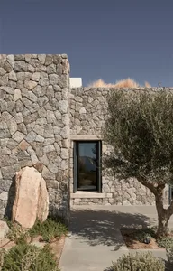 A residential house with walls constructed of irregularly shaped stone blocks, featuring a single glass door and a pathway le