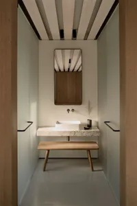 A modern minimalist bathroom featuring a concrete countertop and bench, with a sleek white sink and minimalist mirror.