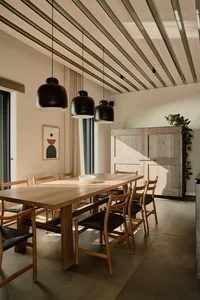 A modern minimalist dining room featuring a wooden table and chairs, with a wooden ceiling and pendant lights