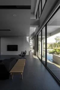 Minimalist living room with concrete floor, black furniture, and large windows showing outdoor greenery.