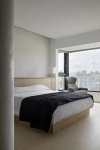 A minimalist bedroom featuring a wooden bed with a concrete headboard, black and white bedding, and a modern armchair next to