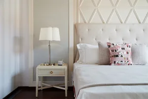 A cozy, modern bedroom featuring a white upholstered bed with a textured tufted headboard, set against a soft, patterned tile
