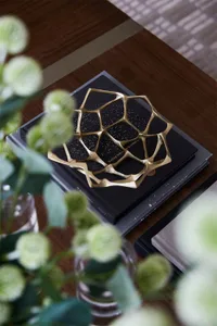 A modern, geometric metal decorative object placed on a book on a wooden surface.