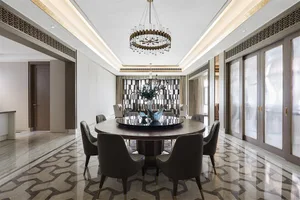 Modern dining room with a round table, chairs, and a chandelier hanging from the ceiling. The floor is made of marble with a 