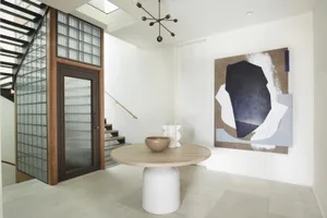 A modern entrance hall featuring a white table with a bowl and vase, complemented by a large abstract black and white wall ar