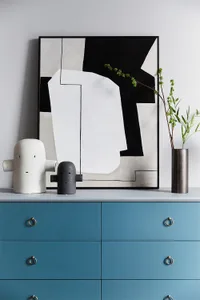 A blue dresser with ceramic storage objects and a black and white abstract painting.