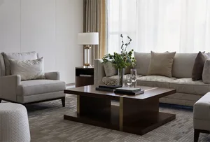 A modern living room featuring a wooden coffee table with books and flowers, a beige armchair, and a white sofa with throw pi