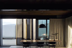 Modern living room with a wooden table and chairs, large windows, and a hanging lamp.