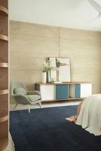 A minimalist bedroom featuring a wooden storage unit, a fabric armchair, and a navy blue rug.