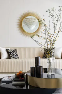 A modern minimalist living room featuring a metallic coffee table, a chandelier, and a sunburst mirror.