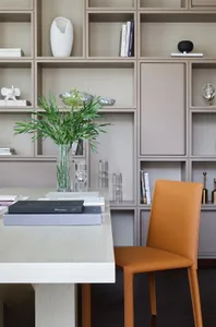A minimalist office with a white desk, brown leather chair, and glass shelves.