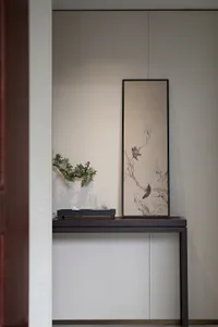 A minimalist console table with a wooden frame and a decorative wallpaper backdrop, featuring a black metal tray holding vari