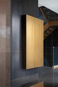 A modern, metallic cabinet mounted on a dark, textured wall.
