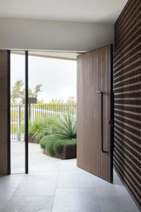 Modern minimalist entrance with a wooden door and steel frame, featuring a sleek design and a view of an outdoor garden with 