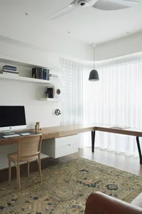 A minimalist home office featuring a wooden desk, leather armchair, and patterned rug.
