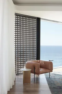 A modern residential interior featuring a sleek, brown leather armchair, a wooden side table, and a large window with ocean v