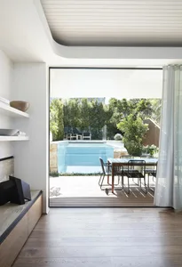 Modern residential pool deck featuring wood, glass fence, and greenery.