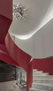 Modern staircase with red handrails and terrazzo stairs, featuring a metallic sculpture on the floor.