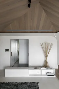 A minimalist interior space with white flooring, featuring a modern floating shelf and a collection of bamboo poles against a