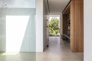 A minimalist office interior with concrete walls and floor, featuring a desk and chair, and large windows with a view of gree