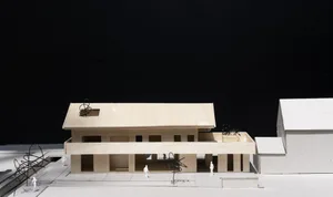 A wooden architectural model of a modern building with an open floor plan and outdoor seating.