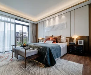 A modern bedroom with minimalist design, featuring a large bed with various pillows, a wooden ottoman, and a large window wit