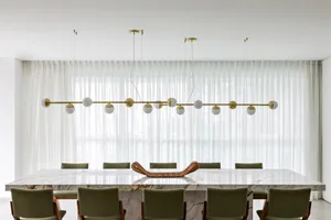 Modern dining room featuring a large table made of marble and a hanging light fixture with spherical bulbs.
