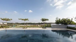 A modern exterior garden with a blue tiled pool, concrete tiles, and a view of distant trees and sky.