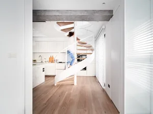 A modern kitchen with wooden flooring, metal railings, and marble countertops, featuring a spiral staircase.