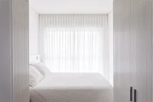 A minimalist bedroom with a white bed, curtains, and wooden walls.