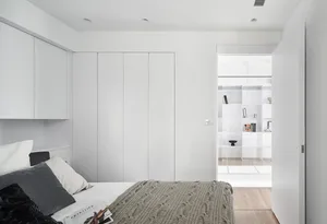 A modern minimalist bedroom featuring white cabinets and wooden floor with a comfortable bed.