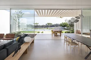 A modern minimalist living room with concrete flooring, a large glass wall, and a sleek, contemporary sofa.