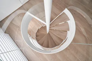 A modern, circular staircase featuring wooden steps and glass railings within a contemporary architectural setting.