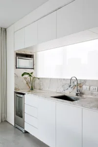 A modern, industrial residential kitchen with marble countertops and white cabinetry, featuring a sink, microwave, and minima