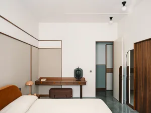 A minimalist bedroom featuring a modern desk and chair, with a bed in the foreground.