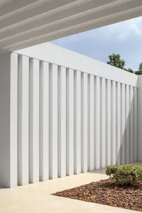 A minimalist concrete wall with vertical slats under a covered patio area.
