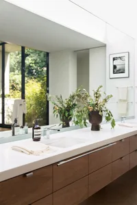 The image features a modern bathroom with natural wood cabinetry and marble countertops, adorned with greenery and elegant de