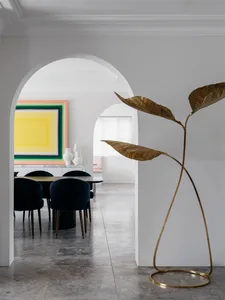Modern dining room with a gold leaf floor lamp, black chairs, and a colorful abstract painting.